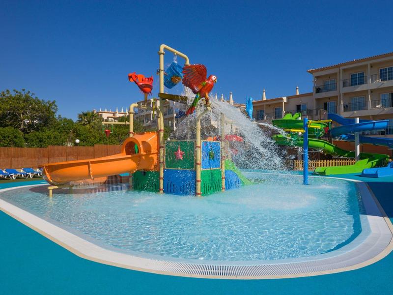Kinder-Wasserpark mit bunten Rutschen und Wasserspielen vor einem Hotelgebäude.