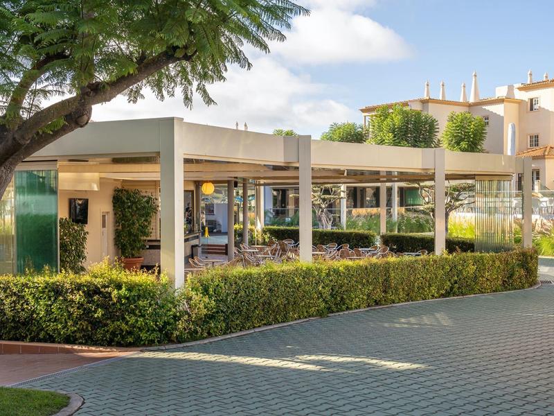 Moderner Hotelbereich mit überdachter Terrasse und gepflegtem Garten unter blauem Himmel.