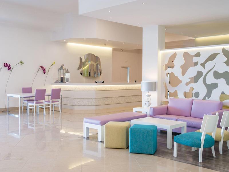 Hell eingerichteter moderner Hotel-Lounge-Bereich mit bunten Sitzmöbeln und skulpturaler Wandverzierung.