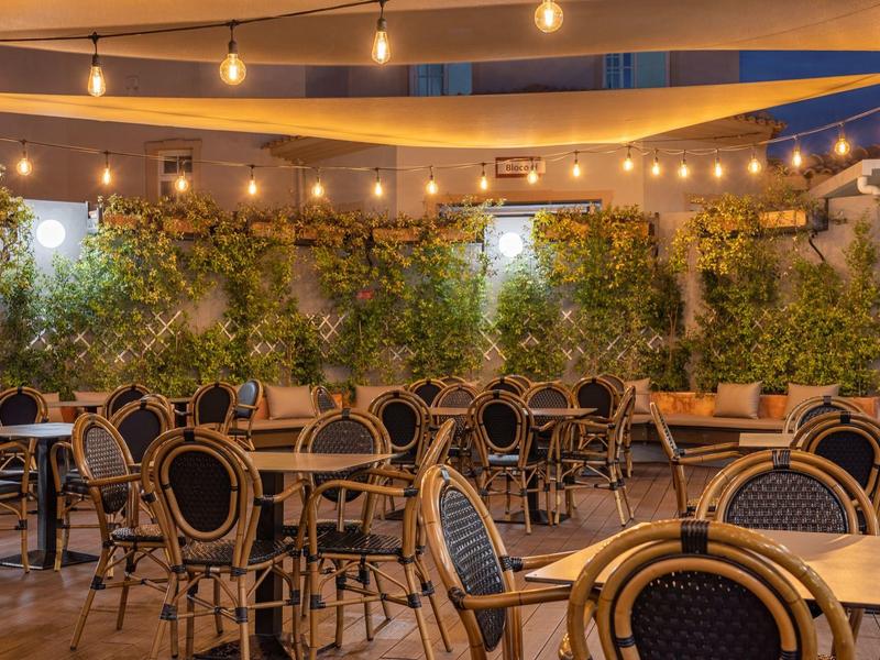 Beleuchtete Außenterrasse mit Tischen und Stühlen vor einer begrünten Wand in einem Hotel.