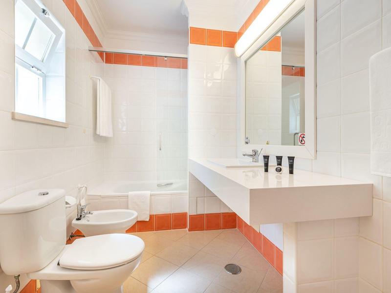 Helles Badezimmer mit Toilette, Bidet, Badewanne und breitem Waschbecken mit Spiegel.