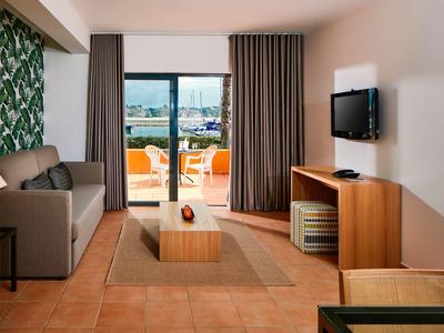 Helles Wohnzimmer mit grauem Sofa, Holzmöbeln und Zugang zu Balkon mit Sitzgelegenheiten.