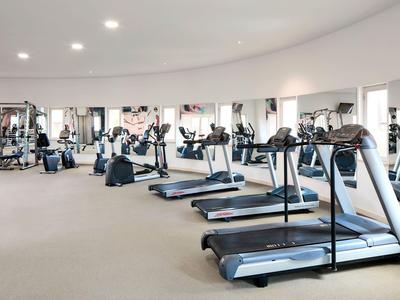 Heller Fitnessraum mit mehreren Laufbändern und anderen Trainingsgeräten in einem Hotel.