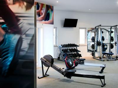 Moderner Fitnessraum mit Rudergerät, Gewichten und Krafttrainingsgeräten in hellem Raum.