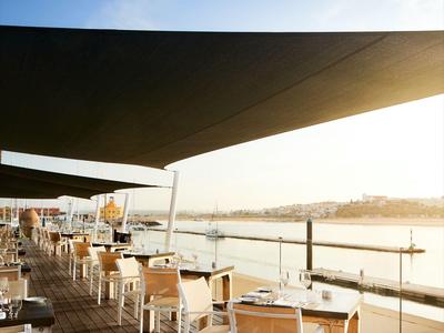 Terrasse mit Holzboden und Tischen mit weißen Stühlen, Blick auf Wasser bei Sonnenuntergang