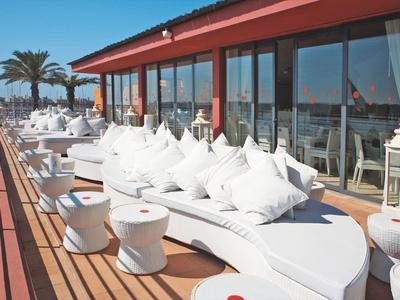 Moderne Dachterrasse mit weißen loungigen Sitzmöbeln, Holzboden und Glasfront bei Sonnenschein.