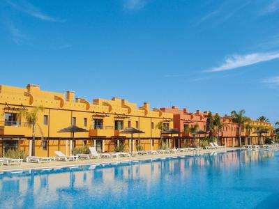 Großer blauer Pool vor gelben und orangenen Reihenhäusern unter blauem Himmel mit wenigen Wolken.