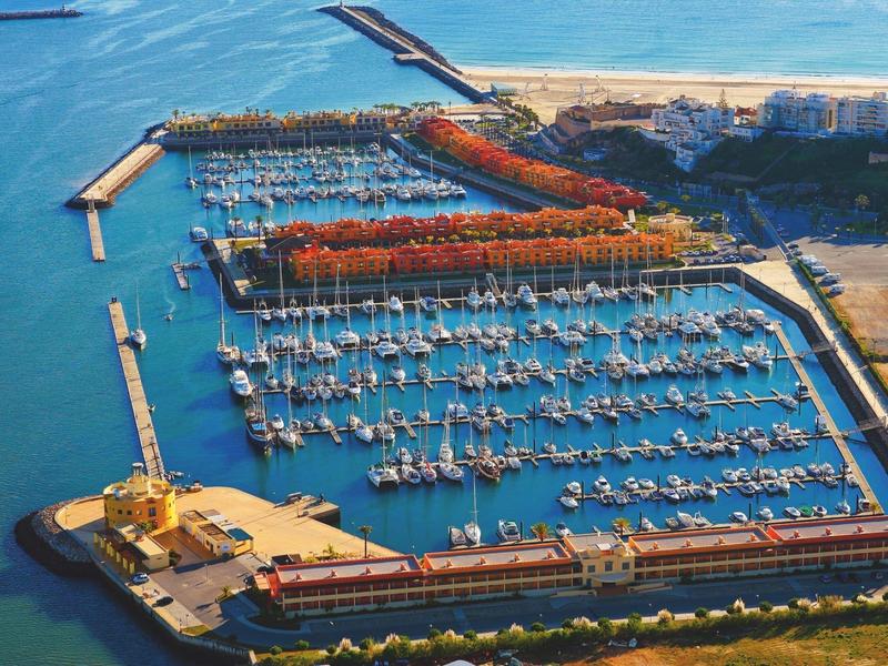 Luftaufnahme eines Yachthafens mit vielen Segelbooten und Bootsstegen, umgeben von Wasser und Küste.