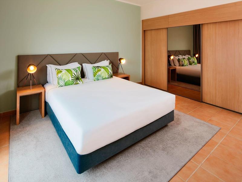 Schlichtes Schlafzimmer mit großem Bett, Holzkleiderschrank und grüner Wand.