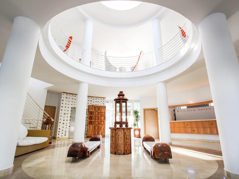 Heller, runder Raum mit hohen weißen Säulen, Holzmöbeln und offener Galerie im Obergeschoss.