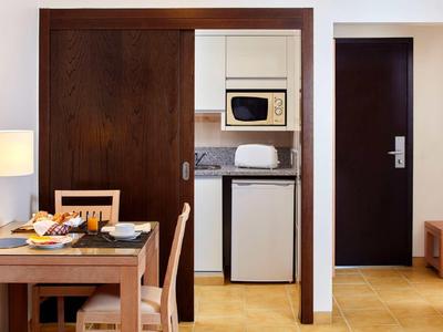 Kleine Küchenzeile mit Mikrowelle, Toaster und Kühlschrank neben einem dunklen Holztisch und Stühlen.