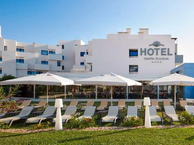 Hotelgebäude in Weiß mit Sonnenschirmen und Liegestühlen vor einer grünen Rasenfläche.