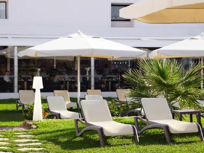 Mehrere Liegestühle und Sonnenschirme auf einer grünen Wiese vor einem Hotelgebäude.