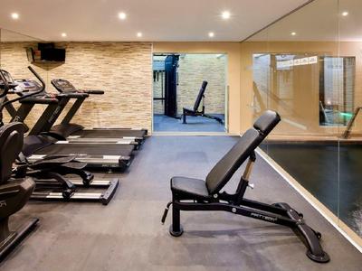 Fitnessraum mit Laufbändern, Trainingsbank und Spiegelwand, heller Steinwand und Schwimmbecken.