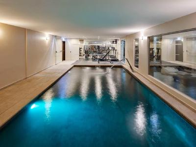 Innen-Pool mit blauem Wasser, beige Fliesenboden und großen Spiegeln an der rechten Wand.