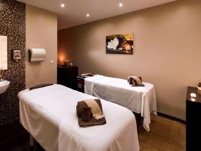 Zwei Massageliegen mit weißen Tüchern in einem warm beleuchteten Raum mit braunen Wänden.