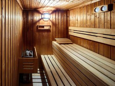Sauna mit hellen Holzplatten, mehrstufigen Holzliegen und Metallofen mit heißen Steinen.