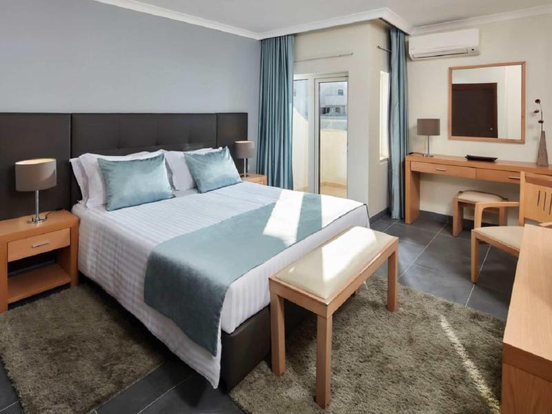 Gemütliches Schlafzimmer mit großem Bett, Holzmöbeln und Teppich in neutralen Farbtönen.