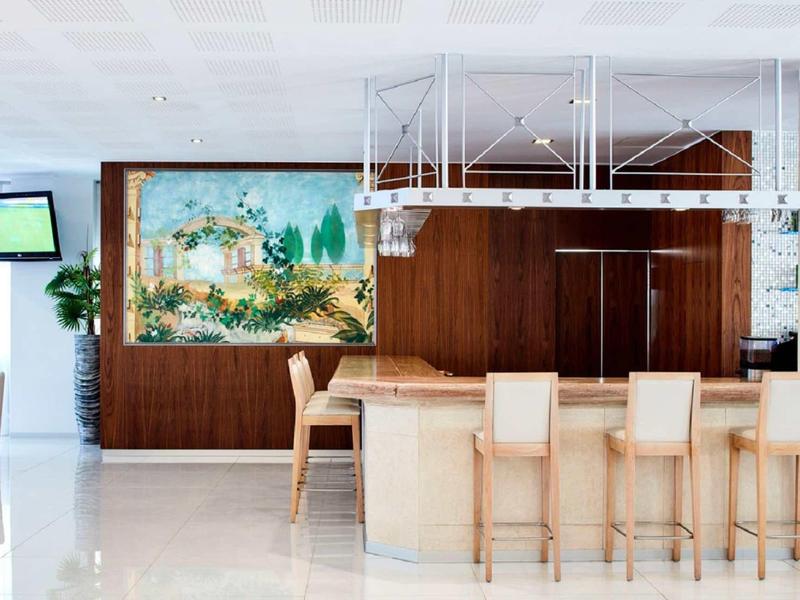 Moderner Raum mit hellem Thekenbereich, sechs Barhockern und großem farbenfrohem Bild an Wand.