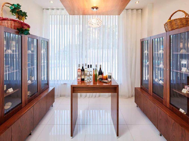 Heller Raum mit Holzvitrinen, zentraler Tisch und großen Fenstern mit weißen Gardinen.