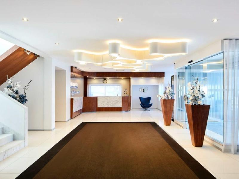 Heller Hotellobby-Eingangsbereich mit braunem Teppich, Holztheke und moderner Beleuchtung.