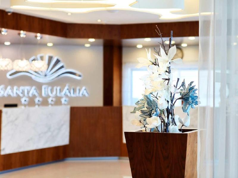 Moderne Hotel-Lobby mit Holzverkleidung, Rezeption und Blumendekoration im Vordergrund.