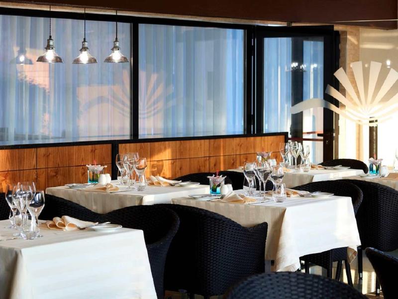 Eleganter Speiseraum mit gedeckten Tischen, weißen Tischdecken, schwarzen Stühlen und großen Fenstern.