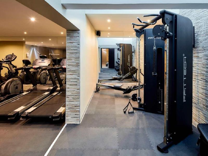 Moderner Fitnessraum mit Laufbändern, Kraftgeräten und Spiegeln, helle Wände, grauer Boden.