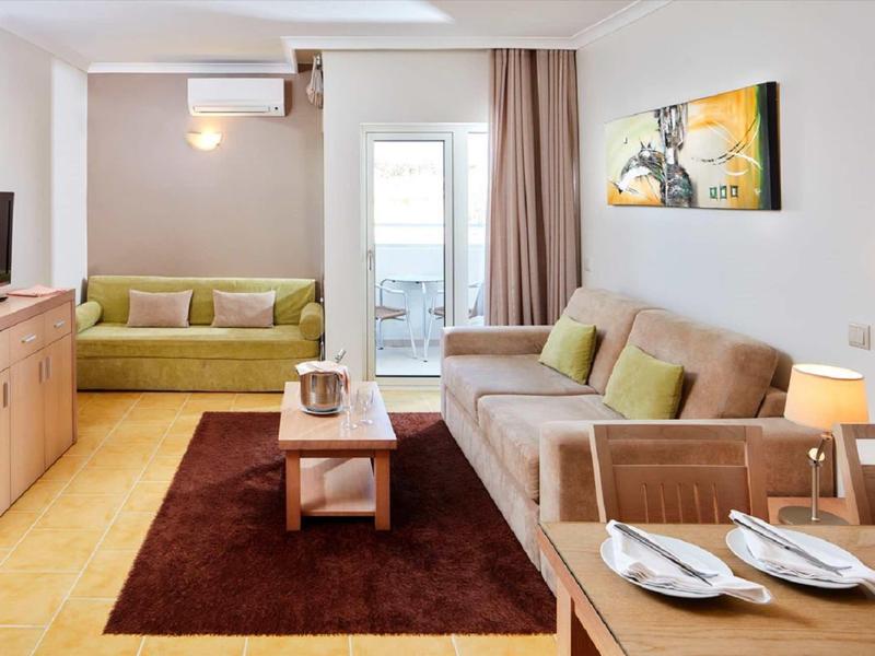 Hell eingerichtetes Wohnzimmer mit grauem Sofa, grünem Sessel, braunem Teppich und Holzmöbeln.