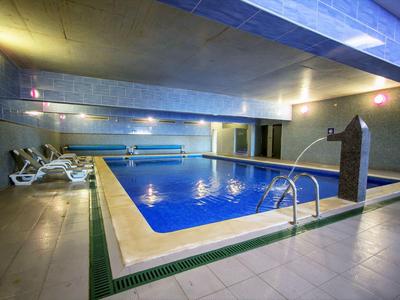 Innenhallen-Schwimmbad mit blauem Wasser, weißen Liegestühlen und gedämpfter Beleuchtung.