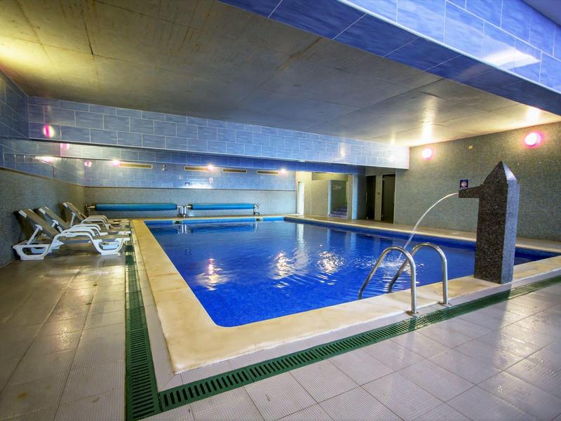 Innenhallen-Schwimmbad mit blauem Wasser, weißen Liegestühlen und gedämpfter Beleuchtung.