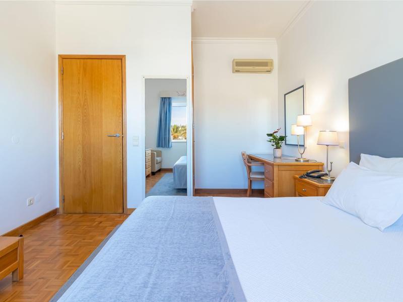 Helle, moderne Schlafzimmer mit Bett, Holztür, Schreibtisch und Luftklimaanlage an der Wand.