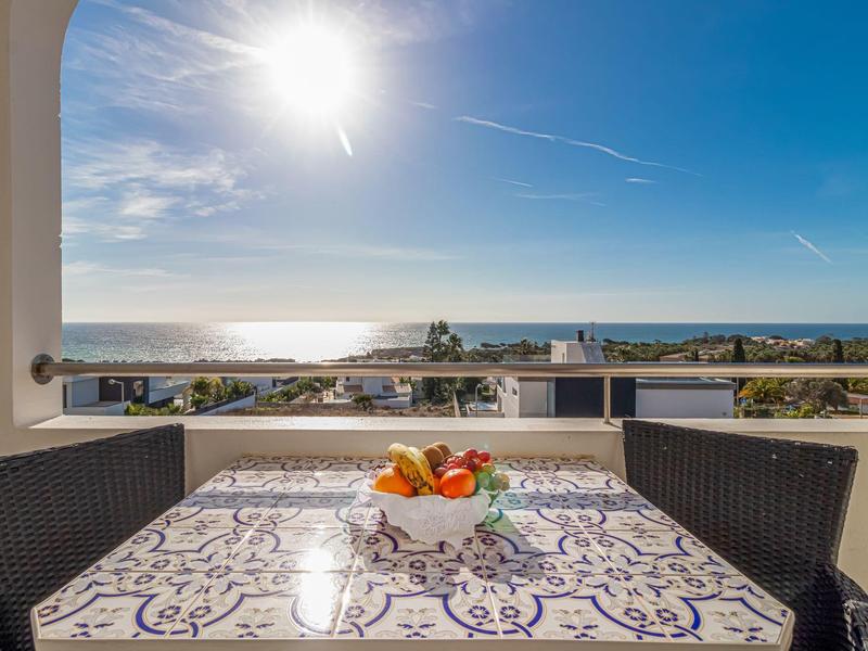 Balkon mit gemustertem Tisch, Obstschale und zwei Stühlen, Meer und Himmel im Hintergrund.