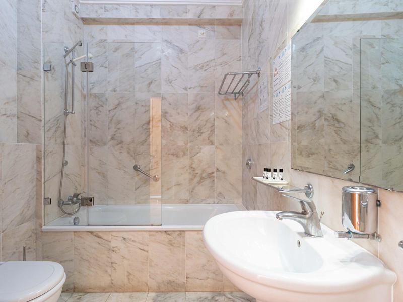 Helles Badezimmer mit Marmorwänden, Badewanne, Waschbecken, Spiegel und weißen Sanitäranlagen.