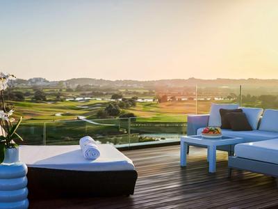 Terrasse mit Holzdeck, modernem Loungemöbel und weitem Blick auf grüne Landschaft bei Sonnenuntergang.