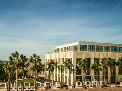 Moderner Bürokomplex mit vielen Fenstern, umgeben von Palmen und blauer Himmel im Hintergrund.