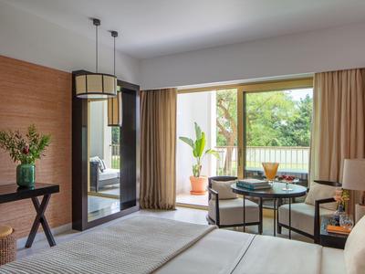 Lichte hotelkamer met tweepersoonsbed, zithoek, grote spiegel en balkon met planten.