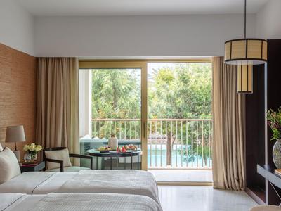 Hotelkamer met tweepersoonsbed, zithoek en balkon met uitzicht op zwembad.