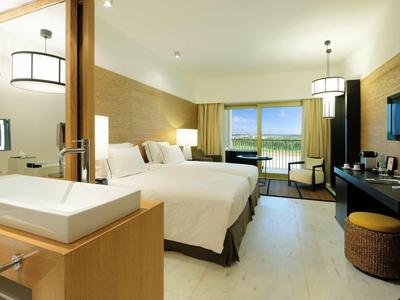 Modernes Hotelzimmer mit zwei Betten, großem Fenster, Fernseher und Badezimmer im Vordergrund.