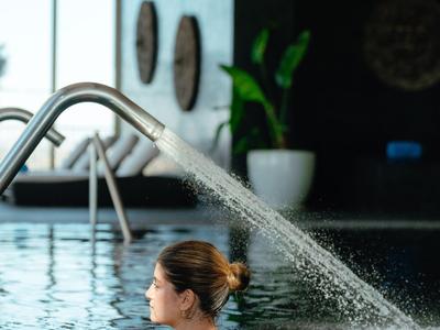 Vrouw ontspant in hotelzwembad met waterstraal en modern interieur op de achtergrond.