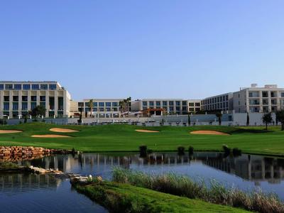 Großes, modernes Gebäude am Ufer mit grünem Rasen und Teich unter klarem blauem Himmel.