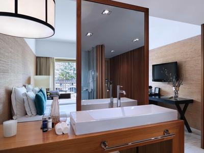 Modernes Hotelzimmer mit Holzvertäfelung, Doppelbett, großem Spiegel und Badewanne im Vordergrund.