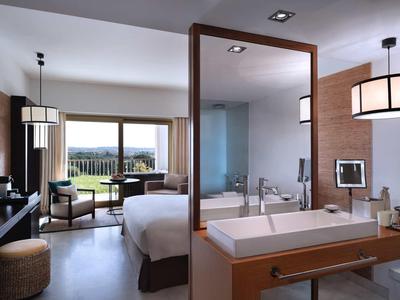 Moderner Hotelraum mit Doppelbett, Sitzecke, Holztrennwand und großem Fenster mit Blick ins Freie.