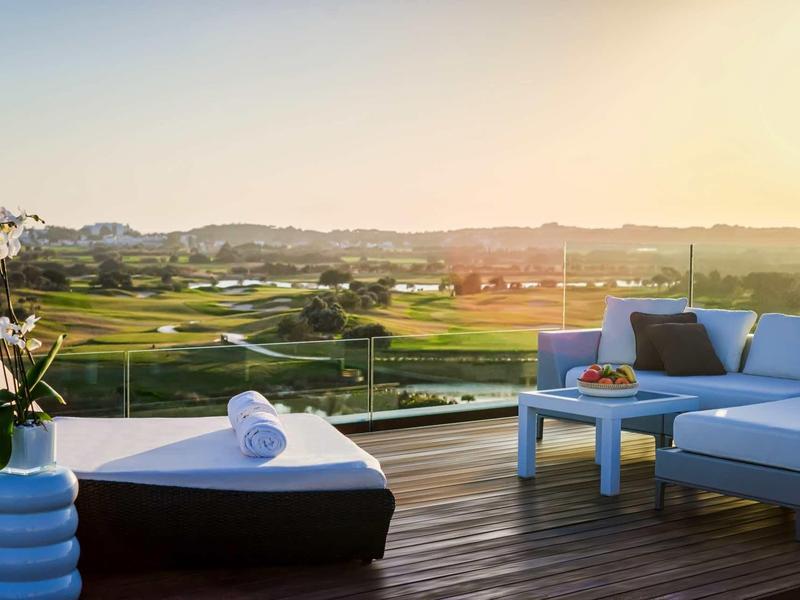 Terrasse mit Holzdeck, modernem Loungemöbel und weitem Blick auf grüne Landschaft bei Sonnenuntergang.