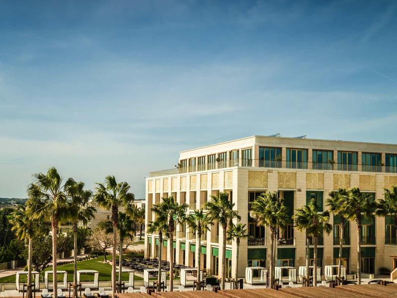 Moderner Bürokomplex mit vielen Fenstern, umgeben von Palmen und blauer Himmel im Hintergrund.