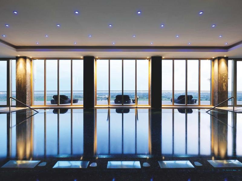 Moderner Innenpool mit großer Fensterfront, sanfter Beleuchtung und ruhiger Wasseroberfläche.