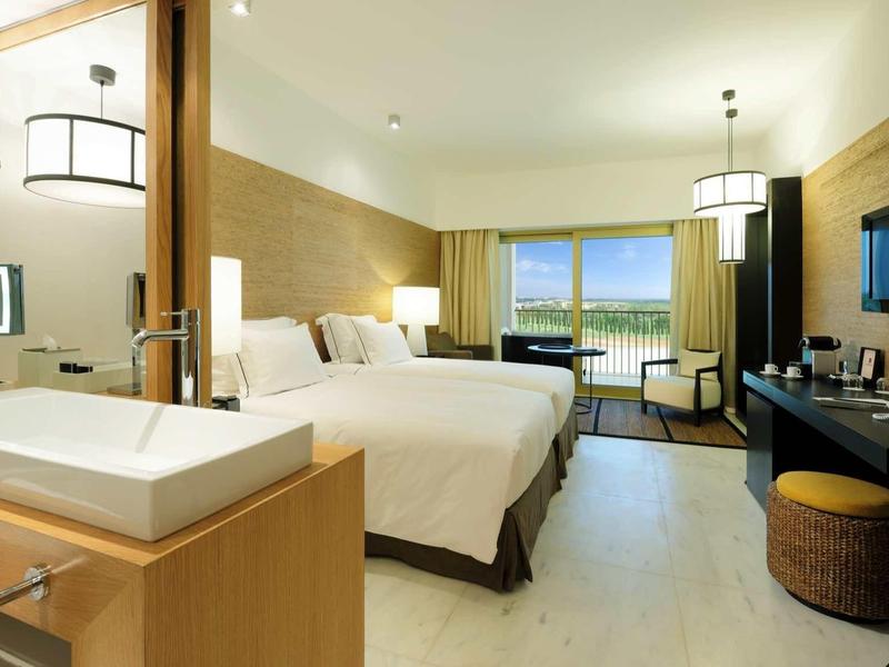 Modernes Hotelzimmer mit zwei Betten, großem Fenster, Fernseher und Badezimmer im Vordergrund.