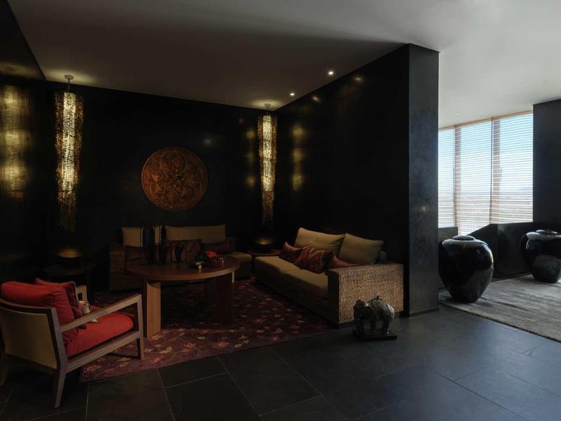 Dunkles Wohnzimmer mit bequemen Sesseln, Sofa, Teppich und großen Fenstern für Tageslicht.