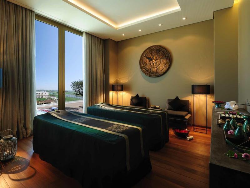 Gemütliches Zimmer mit zwei schwarzen Massageliegen, warmem Licht und großer Fensterfront.