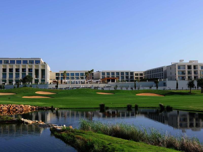 Großes, modernes Gebäude am Ufer mit grünem Rasen und Teich unter klarem blauem Himmel.